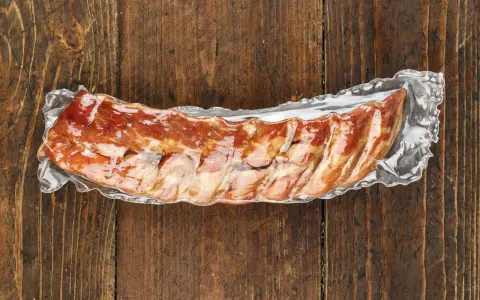 Vakuumverpackte Spareribs sous vide, bereit für die Zubereitung, liegen auf einer rustikalen Holzoberfläche.