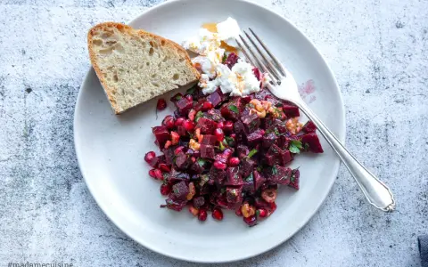 Ein bunter rote beete salat mit Granatapfelkernen, Nüssen und Ziegenkäse, serviert mit Brot.