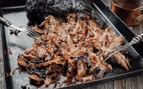 Saftiges Pulled Pork, frisch aus dem Smoker, wird mit Gabeln zerzupft und mit BBQ-Sauce beträufelt.