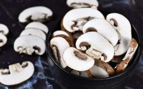 Ein schwarzer Teller mit geschnittenen braunen Champignons. Sie warten darauf, geputzt und zubereitet zu werden.