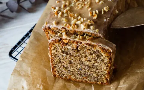 Omas Nusskuchen in Kastenform, mit Zuckerguss und gehackten Nüssen bestreut, wird auf Backpapier präsentiert.