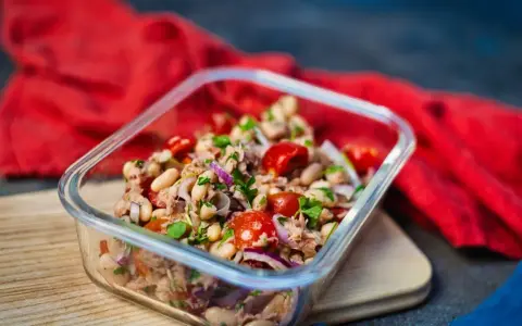 Frischer Thunfischsalat mit weißen Bohnen, Tomaten und roten Zwiebeln in einer Glasbox, bereit zum Mitnehmen.