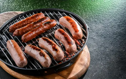 Mehrere Bratwürste brutzeln in der Pfanne auf einem Grill.