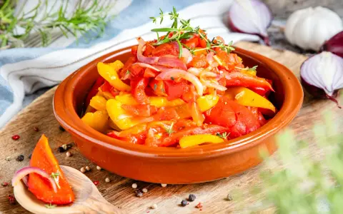 Buntes Peperonata-Gericht im Tontopf, garniert mit Kräutern. Ein Löffel zeigt ein Stück Paprika mit Zwiebeln, perfekt für das original Rezept.