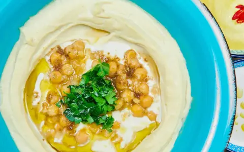 Cremiger Hummus, garniert mit Kichererbsen, Petersilie und Olivenöl. Ein authentisches Hummus Rezept original arabisch, serviert in einer blauen Schüssel.