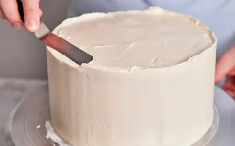 Eine Hand glättet mit einem Spachtel die cremige Buttercreme einer Torte, die für einen Geburtstag bestimmt ist.