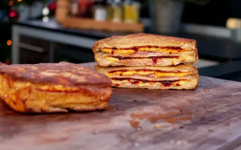 Zwei goldbraune Monte Cristo Sandwiches, gestapelt und mit Käse und Marmelade gefüllt, liegen auf einem Holzbrett.
