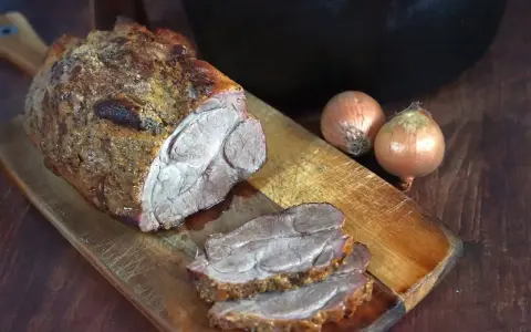 Saftiger Rinderbraten aus dem Dutch Oven, auf einem Holzbrett mit Zwiebeln.