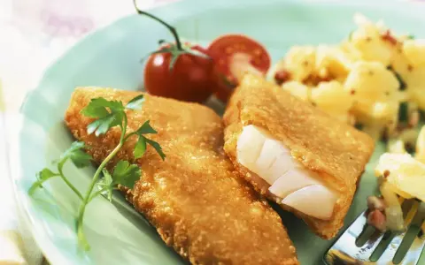 Knuspriger Backfisch mit cremigem Kartoffelsalat und frischer Petersilie, garniert mit Kirschtomaten.