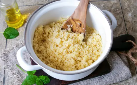 Frisch zubereiteter Couscous als Beilage in einem Topf, daneben ein Glas Öl und Minzblätter.