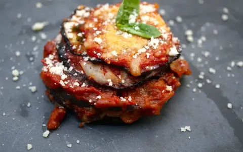 Melanzane alla Parmigiana: geschichtete Aubergine mit Tomatensauce, Käse und Basilikum, bestreut mit Parmesan.