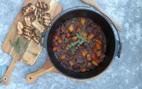 Herzhaftes Rindfleischgulasch im Dutch Oven, mit Kartoffeln, Karotten und Erbsen. Dazu geröstetes Brot. Perfekt für Dutch Oven Rezepte Rind.