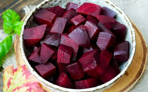 Schüssel mit gewürfelter roter Bete, bereit für die Kochzeit. Frische grüne Blätter und ein Herbstblatt liegen daneben.
