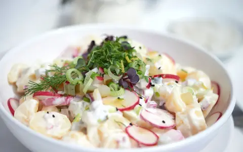 Ein cremiger Kartoffel Radieschen Salat, garniert mit frischen Kräutern und Frühlingszwiebeln.