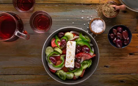 Frischer griechischer Salat mit Feta, Oliven, Tomaten, Gurken und Paprika, serviert mit Rotwein und Gewürzen.