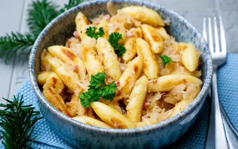 Schupfnudeln mit Sauerkraut, garniert mit Petersilie, in einer blauen Schüssel. Ein Klassiker der deutschen Küche.