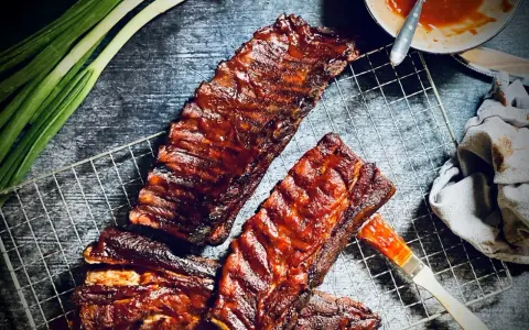 Saftige spareribs grillen holzkohle, mit BBQ-Sauce bestrichen, bereit zum Genuss. Grüne Frühlingszwiebeln und ein Pinsel liegen daneben.