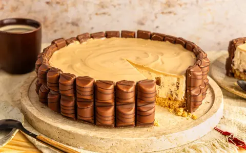 Eine köstliche Kinder Bueno Torte, umrandet von Schokoriegeln, mit einem Stück herausgeschnitten. Daneben eine Tasse Kaffee.