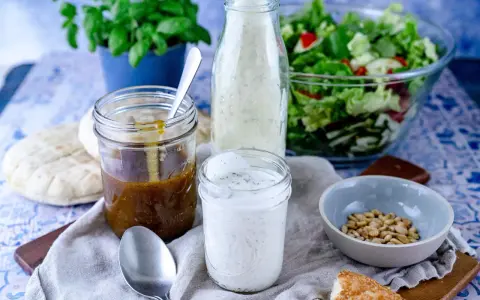 Ein Glas cremiges **ranch dressing** steht neben einem Glas mit brauner Soße, einem Salat und Brot.