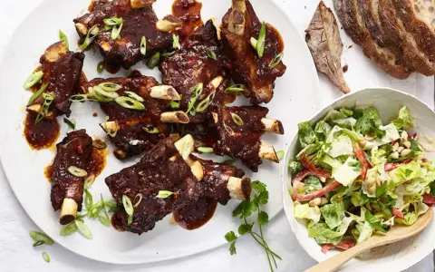 Saftige Spareribs mit BBQ-Sauce und Frühlingszwiebeln, serviert mit einem frischen Salat.