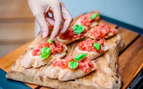 Frische Bruschetta vom Grill, belegt mit Tomaten und Basilikum, wird von einer Hand garniert.