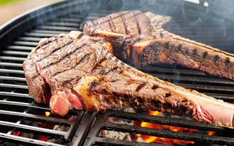 Zwei saftige tomahawk steaks brutzeln auf dem Grill. Rauch steigt auf, die Kohlen glühen.