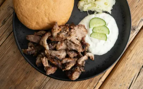 Saftiges Gyros vom Grill mit Tzatziki, Krautsalat und einem Brötchen auf schwarzer Platte.