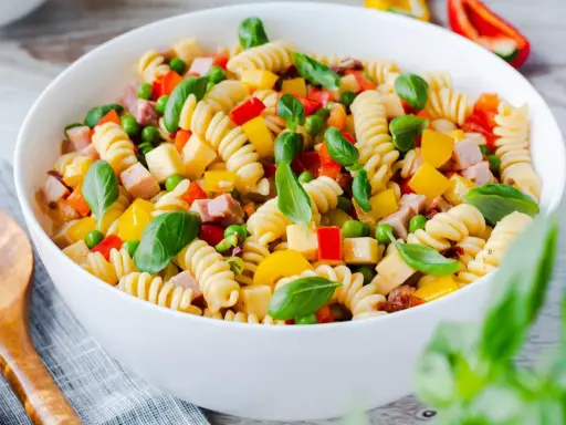 Bester Pasta Salat ohne Mayonnaise: Spiralnudeln mit Schinken, Erbsen, Paprika und Basilikum in einer weißen Schüssel.