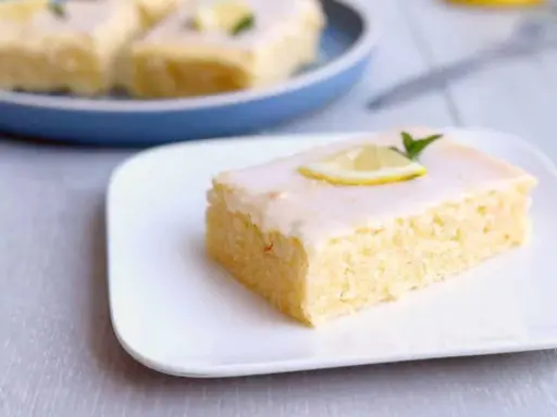 Ein Stück von Omas Zitronenkuchen vom Blech, mit Zuckerguss und Zitronenscheibe garniert.