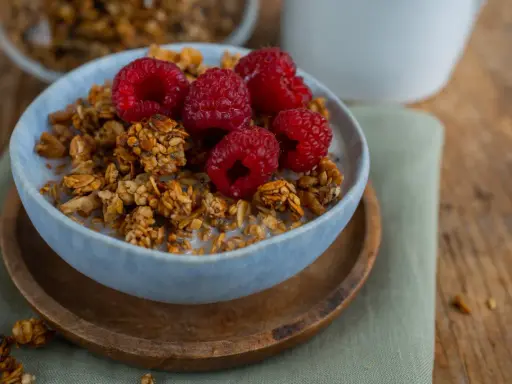 Schüssel mit selbstgemachtem Granola, Milch und frischen Himbeeren. Ein gesunder Start in den Tag!