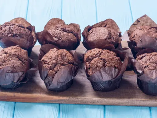 Acht schokoladige Muffins im braunen Papier auf einem Holzbrett. Perfekt für ein schokomuffins rezept.