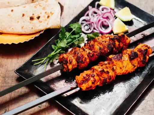 Zwei Spieße mit saftigem Tandoori Chicken, garniert mit Koriander, Zwiebelringen und Zitronenspalten. Dazu Fladenbrot.