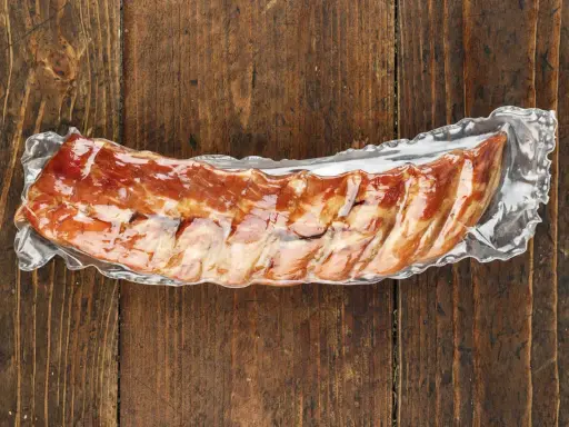 Vakuumverpackte Spareribs sous vide, bereit für die Zubereitung, liegen auf einer rustikalen Holzoberfläche.