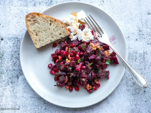 Ein bunter rote beete salat mit Granatapfelkernen, Nüssen und Ziegenkäse, serviert mit Brot.