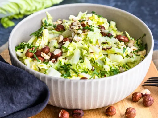 Frischer Chinakohlsalat mit gehackten Haselnüssen und Petersilie, garniert mit ganzen Nüssen.