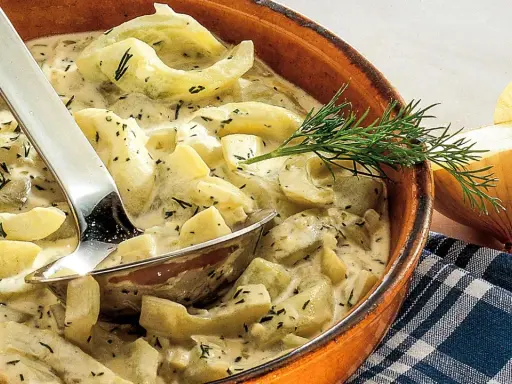 Schmorgurken in cremiger Soße mit Dill, daneben eine Zwiebel. So sehen sie aus, lecker und appetitlich.