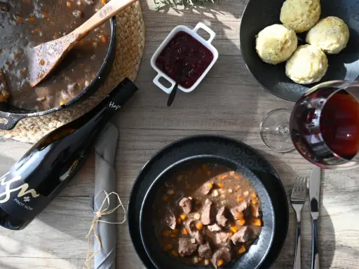 Herzhaftes Wild im Dutch Oven, serviert mit Klößen, Preiselbeeren und einem Glas Rotwein. Ein Festmahl!