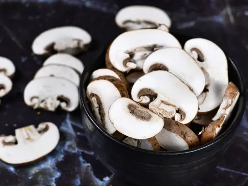 Ein schwarzer Teller mit geschnittenen braunen Champignons. Sie warten darauf, geputzt und zubereitet zu werden.
