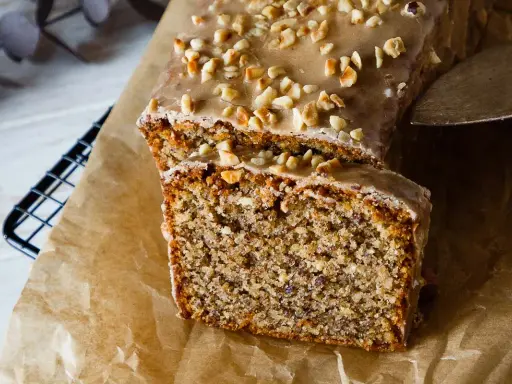 Omas Nusskuchen in Kastenform, mit Zuckerguss und gehackten Nüssen bestreut, wird auf Backpapier präsentiert.