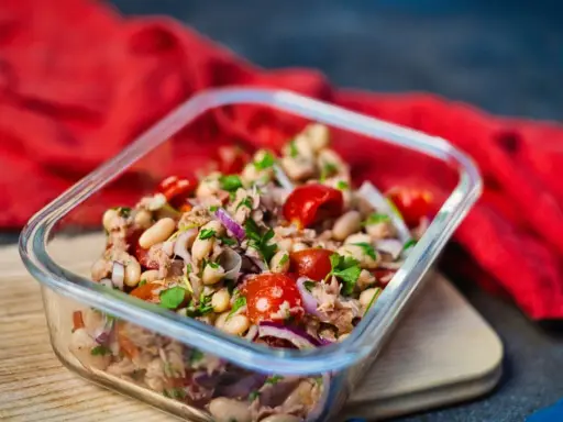 Frischer Thunfischsalat mit weißen Bohnen, Tomaten und roten Zwiebeln in einer Glasbox, bereit zum Mitnehmen.
