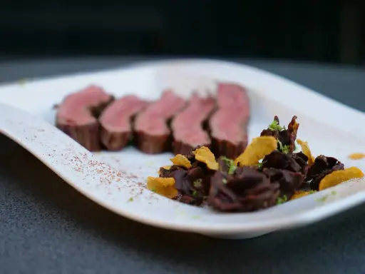 Perfekt zubereitetes Flank Steak, in Scheiben geschnitten, serviert mit einer dunklen Schokoladen-Beilage und knusprigen Chips.