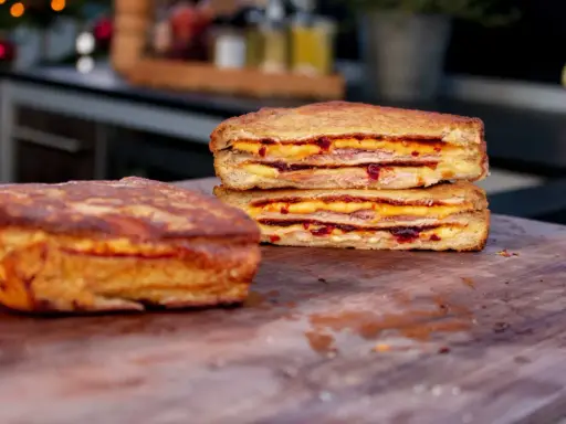 Zwei goldbraune Monte Cristo Sandwiches, gestapelt und mit Käse und Marmelade gefüllt, liegen auf einem Holzbrett.