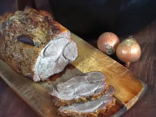 Saftiger Rinderbraten aus dem Dutch Oven, auf einem Holzbrett mit Zwiebeln.