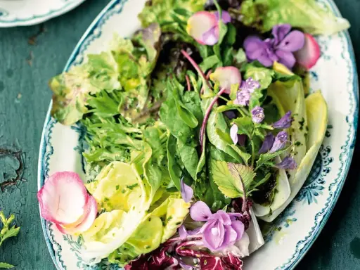 Ein bunter gemischter Salat mit zarten Blüten und Radieschen auf einem verzierten Teller.