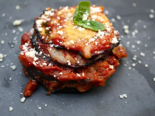 Melanzane alla Parmigiana: geschichtete Aubergine mit Tomatensauce, Käse und Basilikum, bestreut mit Parmesan.