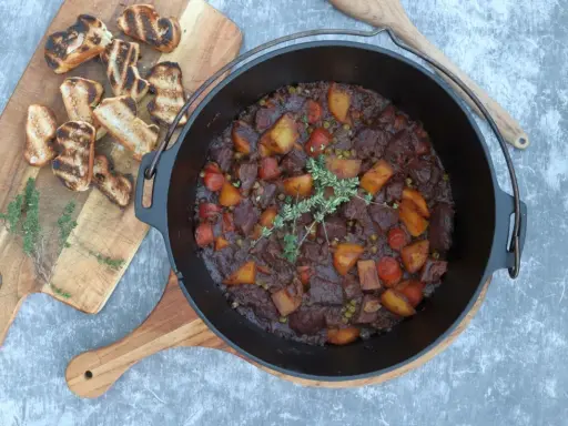 Herzhaftes Rindfleischgulasch im Dutch Oven, mit Kartoffeln, Karotten und Erbsen. Dazu geröstetes Brot. Perfekt für Dutch Oven Rezepte Rind.
