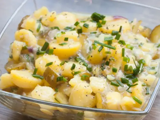 Kartoffelsalat ohne Mayo, mit Gurken, Zwiebeln und Schnittlauch in einer Glasschüssel.