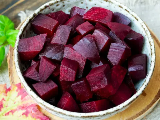 Schüssel mit gewürfelter roter Bete, bereit für die Kochzeit. Frische grüne Blätter und ein Herbstblatt liegen daneben.
