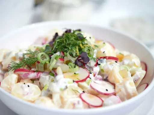 Ein cremiger Kartoffel Radieschen Salat, garniert mit frischen Kräutern und Frühlingszwiebeln.