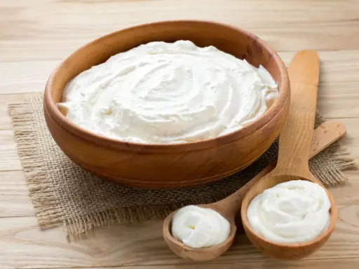 Cremiger Schmand in Holzschale und Löffeln. Ist Schmand gesund? Ja, in Maßen genossen, liefert er Kalzium und Proteine.